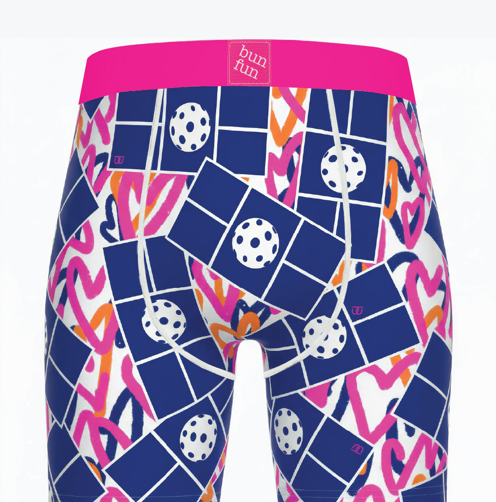 Men's boxer briefs featuring a vibrant geometric pattern of navy blue tiles, white polka dots, pink wavy lines, and orange accents, with a bright pink waistband. The brand name 'bun fun' is visible on the front waistband label.