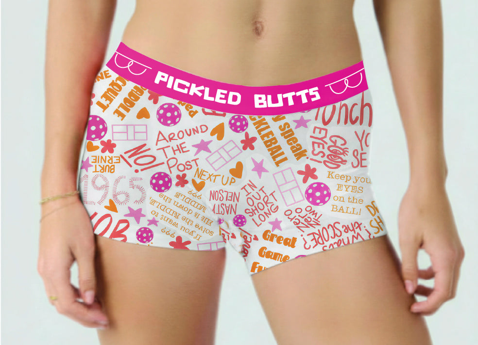 Say What pickleball underwear for women featuring white boxer briefs with a bright pink waistband and an allover retro-style text and graphic print in pink, orange, and purple. The waistband reads 'PICKLED BUTTS'.