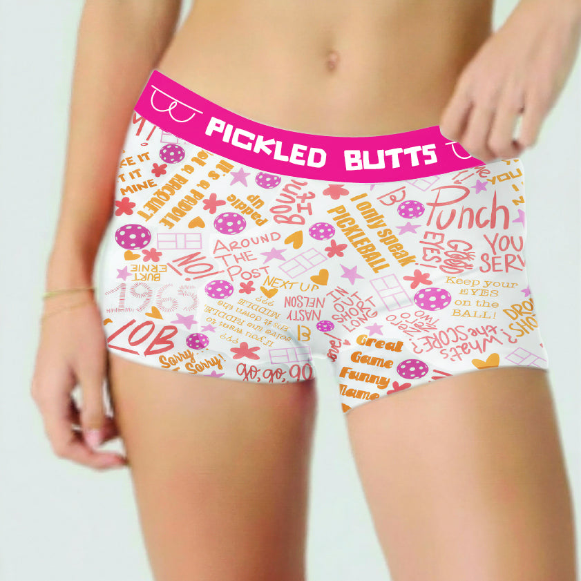 Say What pickleball underwear for women featuring white boxer briefs with a bright pink waistband and an allover retro-style text and graphic print in pink, orange, and purple. The waistband reads 'PICKLED BUTTS'.